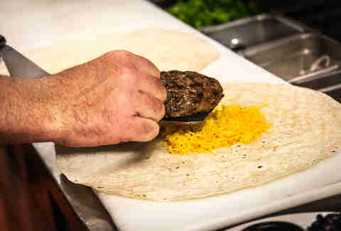 The all beef patty is placed on a bed of shredded cheese on the Supreme Nacho Burger at Slater's 50/50 in Liberty Station San Diego.