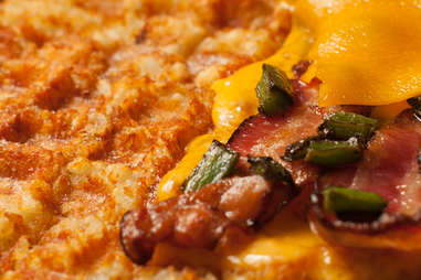 Tater tot waffle topped with bacon and roasted jalapenos to make a grilled cheese — Thrillist Recipes