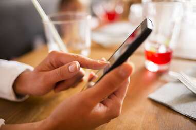 Woman on iPhone at dinner table with drinks