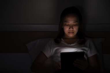 Woman looking at bright iPad in dark bedroom at night