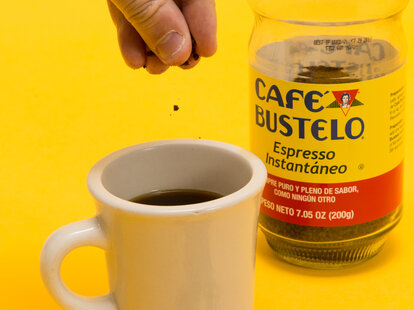 Hand dropping coffee grounds into mug of coffee
