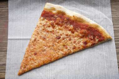 Slice of cheese pizza on thin wax paper
