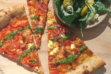 Multiple slices of Mill pizza next to bowl of herbs