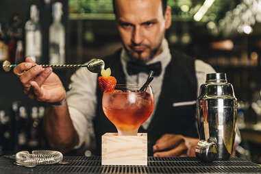 Mixologist placing strawberry garnish on red cocktail