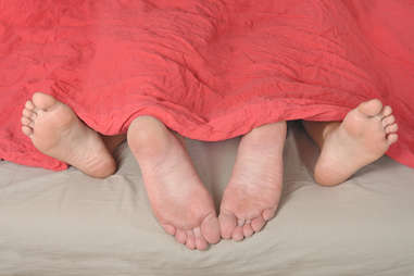 Feet of couple having sex in bed under blanket