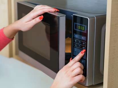 Girl with painted red nails using microwave