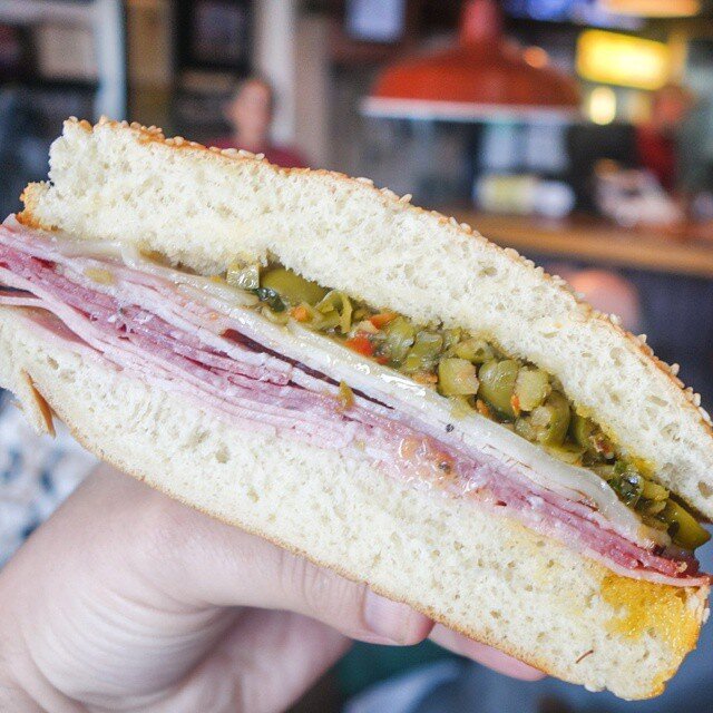 Hand holding Muffaletta sandwich filled with giardiniera