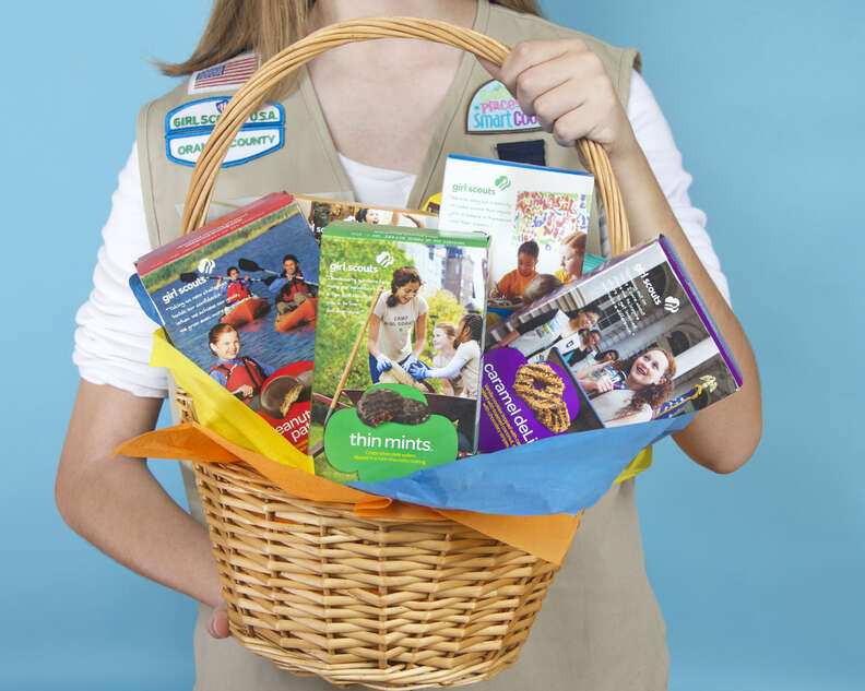 Girl scout carrying a basket full of Girl Scout Cookie boxes
