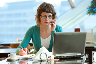 woman at a cafe on her phone with a laptop