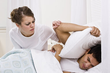 irritated man and woman in bed trying to wake up