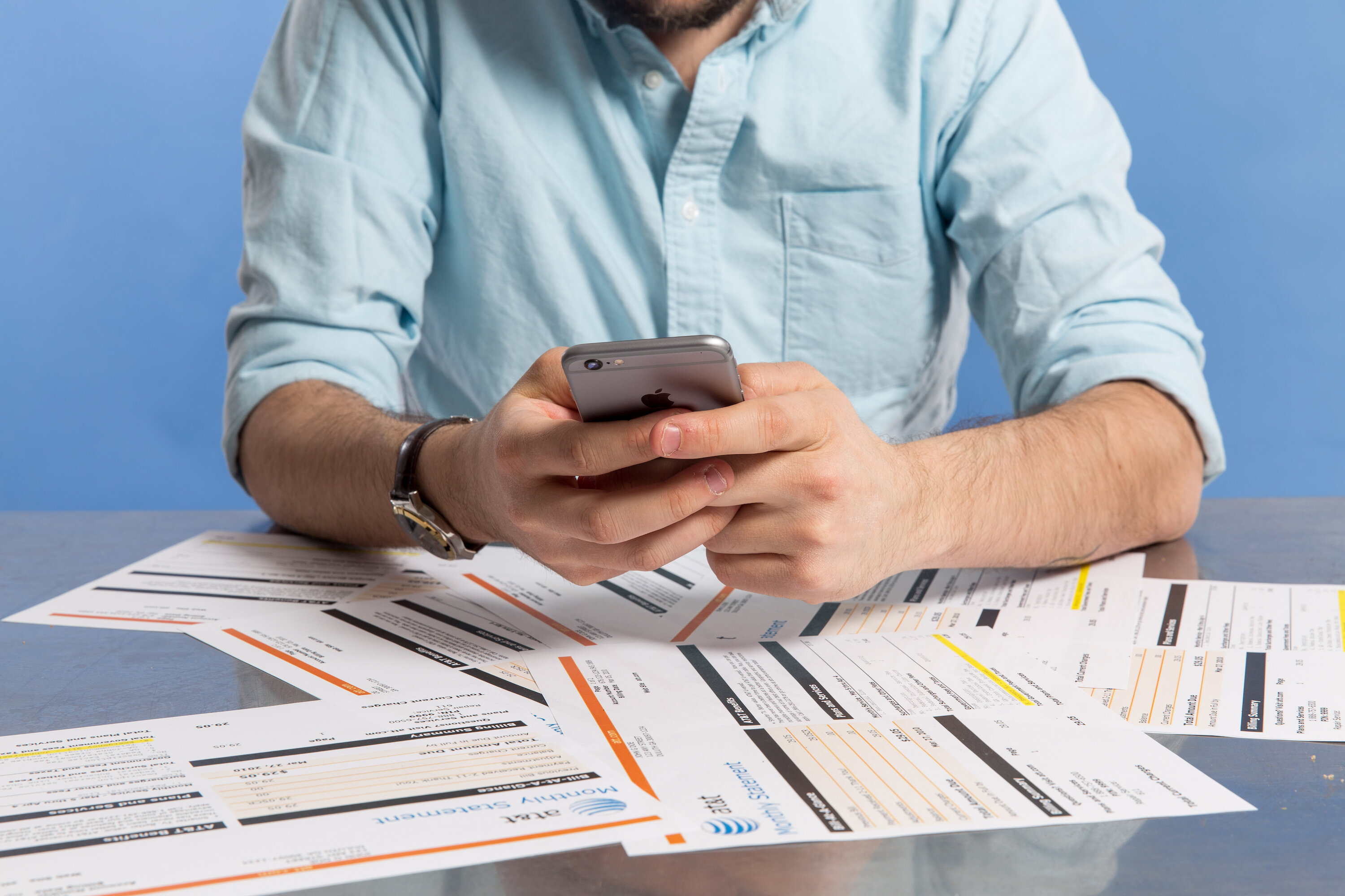 man using iphone 6 above a pile of phone bills