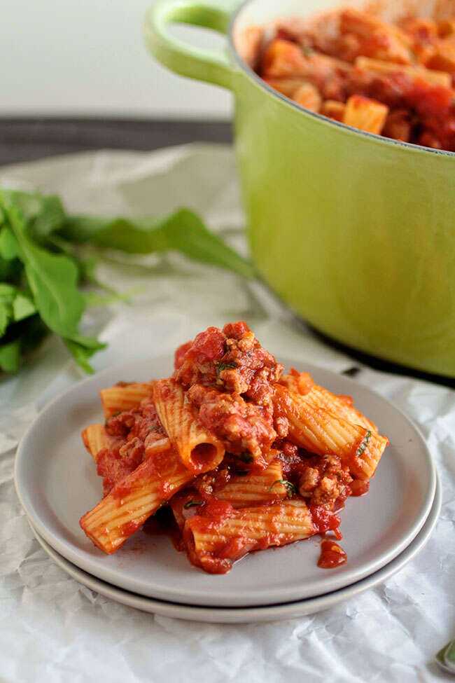 Spicy tomato pasta with sausage and crushed tomatoes on white plate