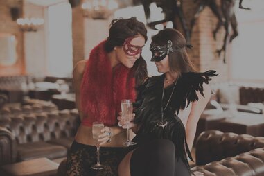 Two women in masks drinking champaign and flirting