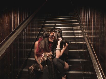 Two women in masks flirting on staircase
