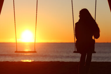lonely woman on swings looking at sunset