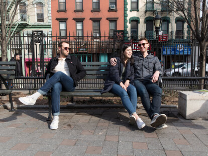 Couple sits on park bench while jealous friend watches