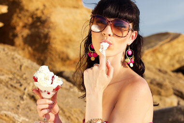 Girl in sunglasses licking whipped cream off her fingers