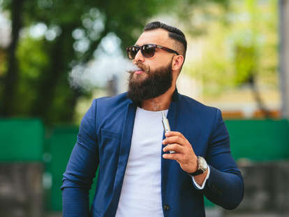 Bearded hipster man smoking vaporizer in public