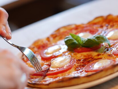 cutting a pizza pie with a knife and fork