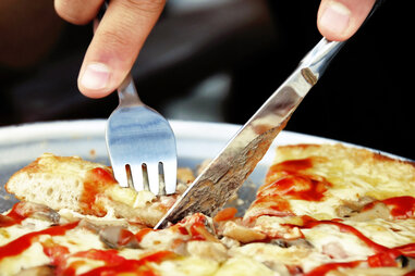closeup of someone cutting a slice of pizza with a knife and fork