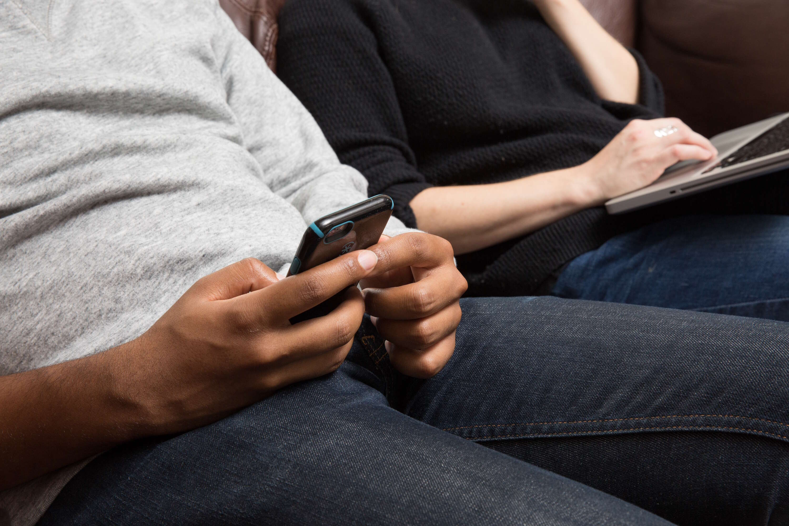man texting next to woman on couch