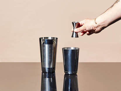 Bartender Holds In Hand Steel Jigger And Pours Drink From Bottle