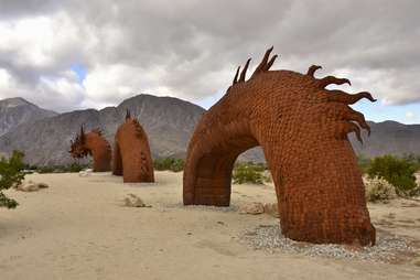 a dragon sculpture diving in and out of the sand in the desert