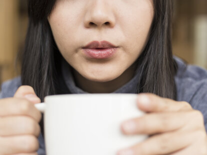 woman blowing on hot coffee