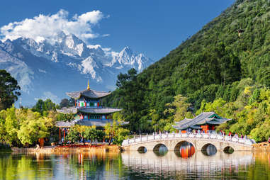 jagged snow-coverec peaks of Jade Dragon Snow Mountain in the background of a bridge in China