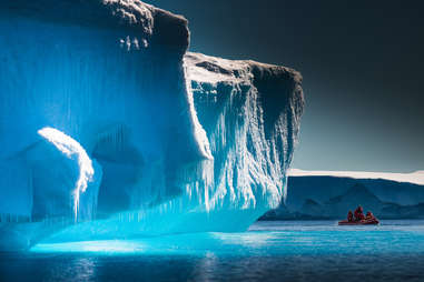 three people in a boat sailing past a giant iceberg