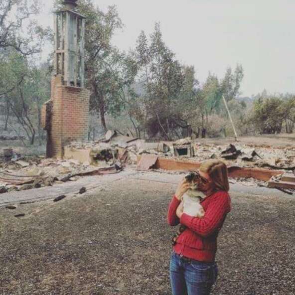 Woman holding cat in front of destroyed house