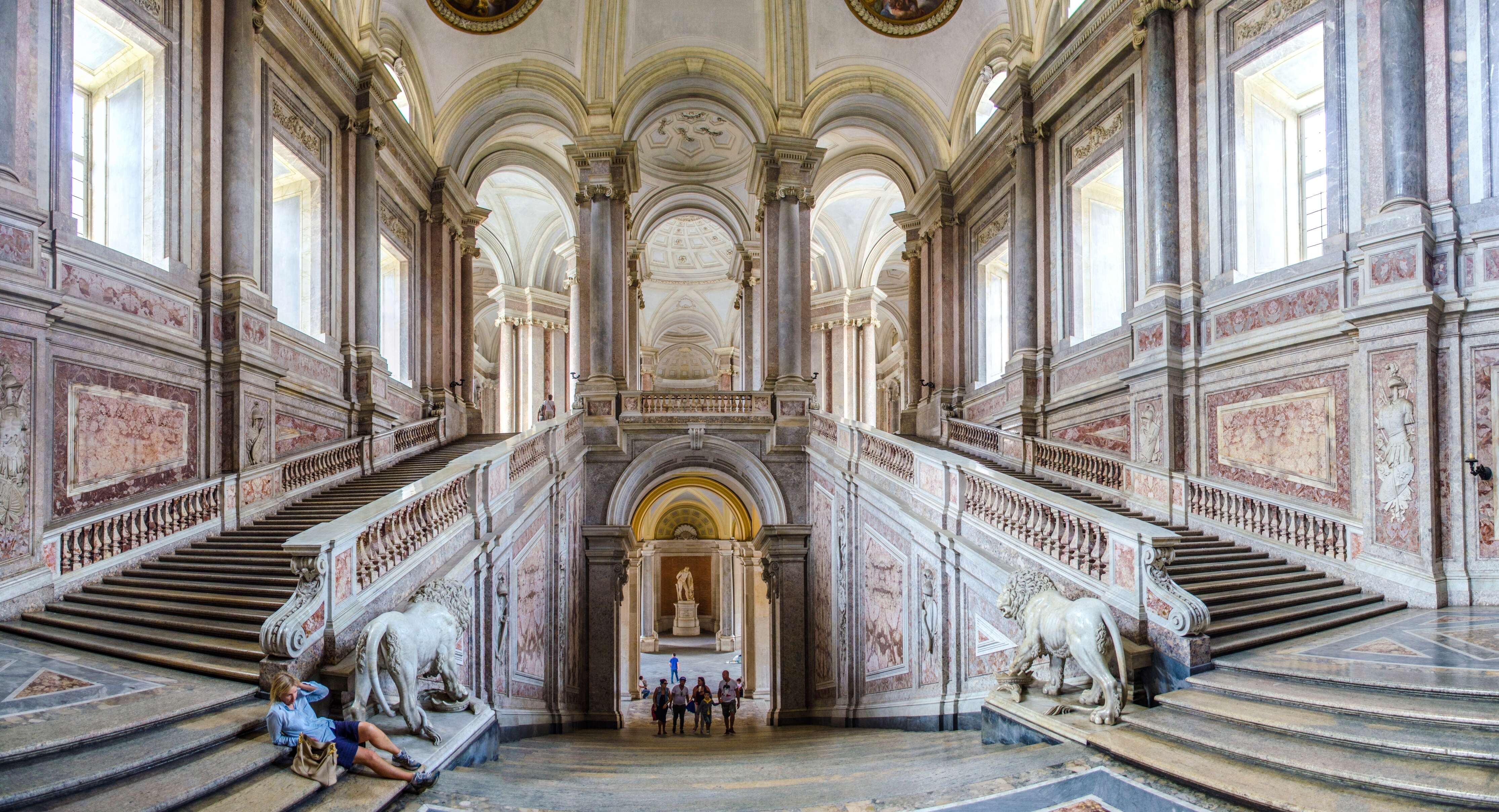 people sit on a double staircase in an ornate Italian palace