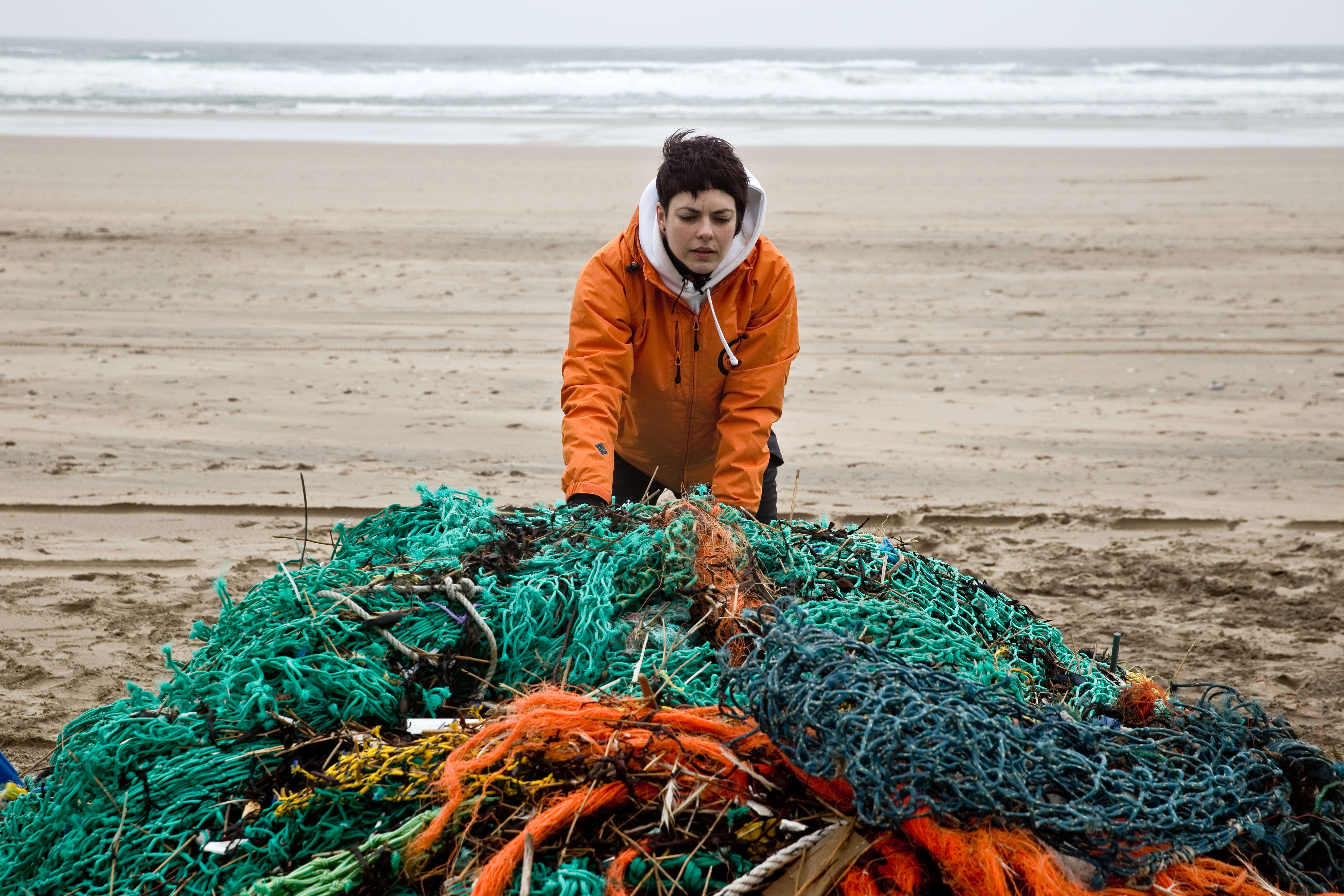 Woman handling a ghost net on a beach 