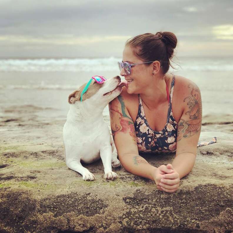 Dog kissing woman while they lay on the beach
