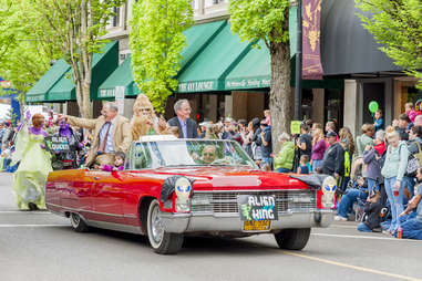 an alien king and sasquatch riding through a crowd of spectators in a red convertible