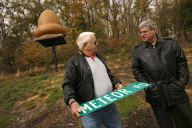 two older men holding a sign reading meteor road