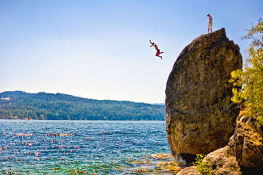 people jumping off a rock into a lake
