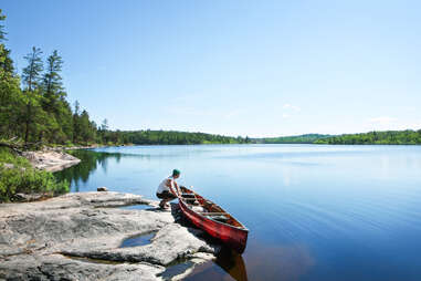 man holding canoe on the shores of wilderness lake