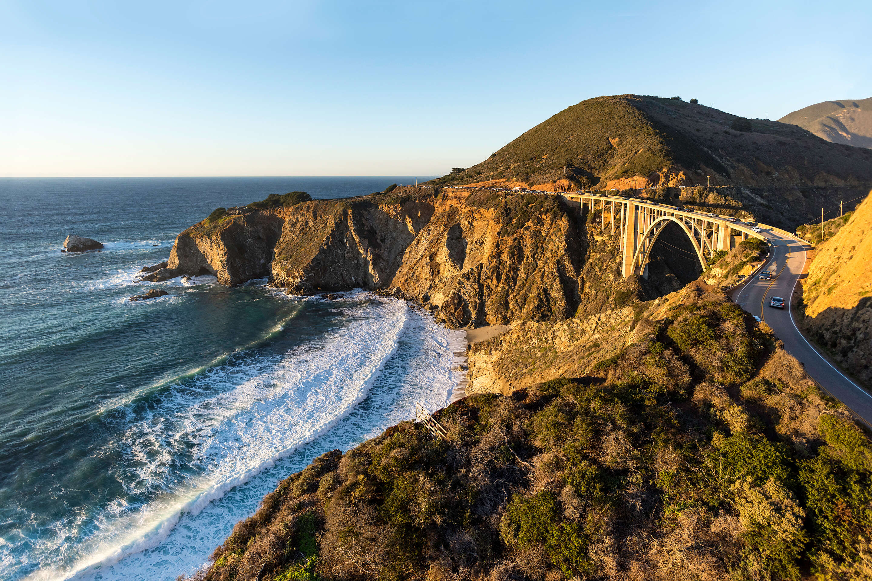 cars on road winding by ocean cliffs