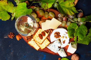white wine, blue cheese, crackers, nuts, and grapes on a platter
