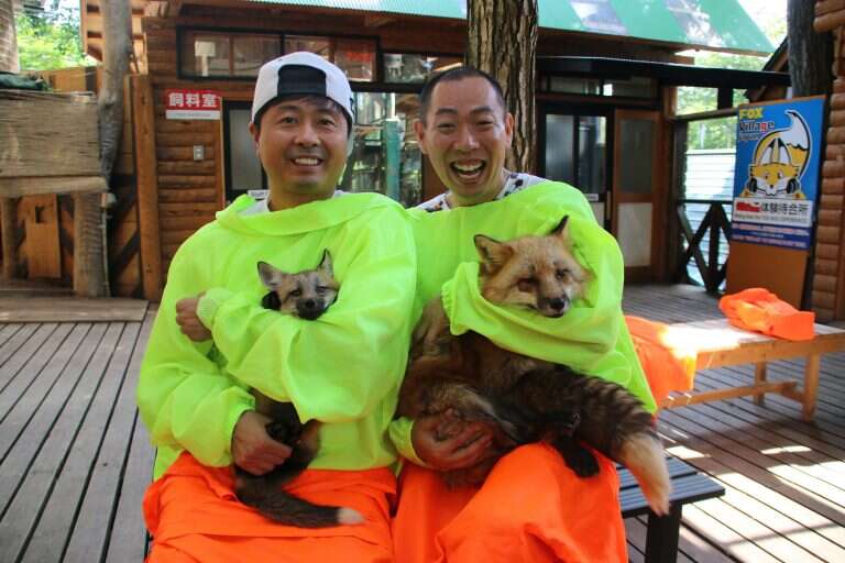 Tourists hold two foxes at Fox Village in Japan