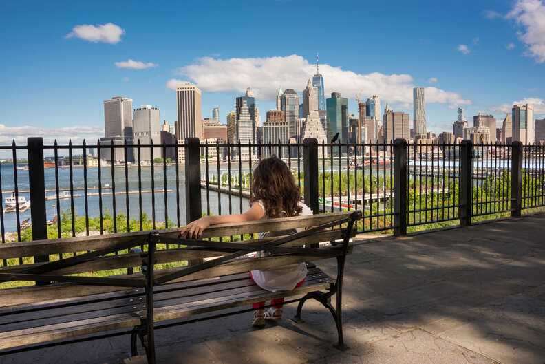 woman sitting on bench on Brooklyn Promenade in front of skyline