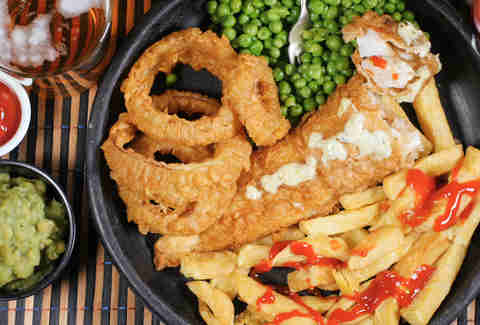 Top down view of an English fish and chips with garden peas, ring onions and mushy peas