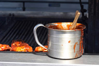 Steel container full of bbq sauce next to a bbq grill
