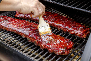 racks of ribs, hand applying bbq sauce on grill