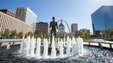 The Runner statue is splashed by the fountain in Kiener Plaza with the Old Courthouse and the Arch framing it in the background.