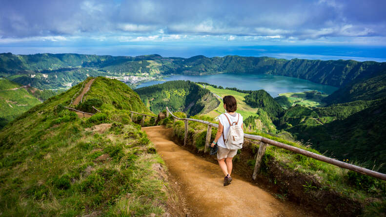 person walking down a mountain trail near lakeside vista