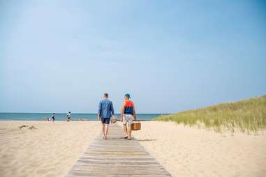 two men walking along a boardwalk toward a beach