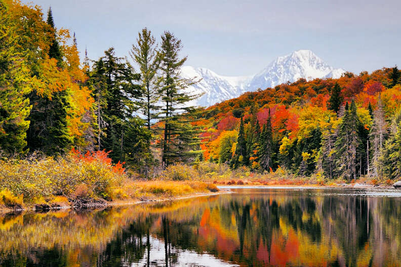 a lake surrounded by colorful trees in fall with a mountain range in the distance