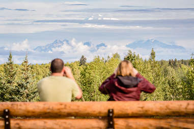 two tourists looking out across trees onto enormous mountains